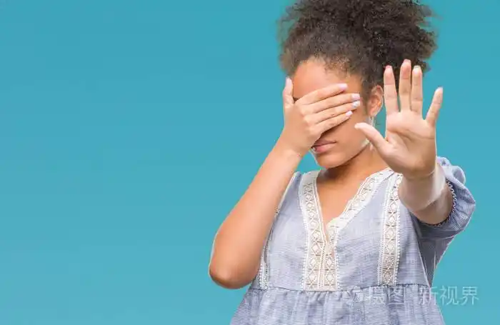 年轻的美国黑人妇女在孤立的背景上用手遮住眼睛,用悲伤和恐惧的表情